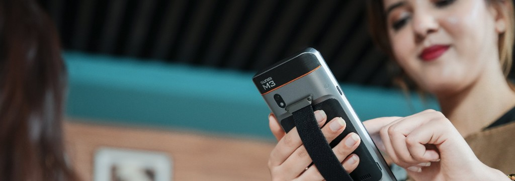 Staff member using a Sunmi M3 mobile handheld terminal with hand strap in a modern retail or hospitality setting